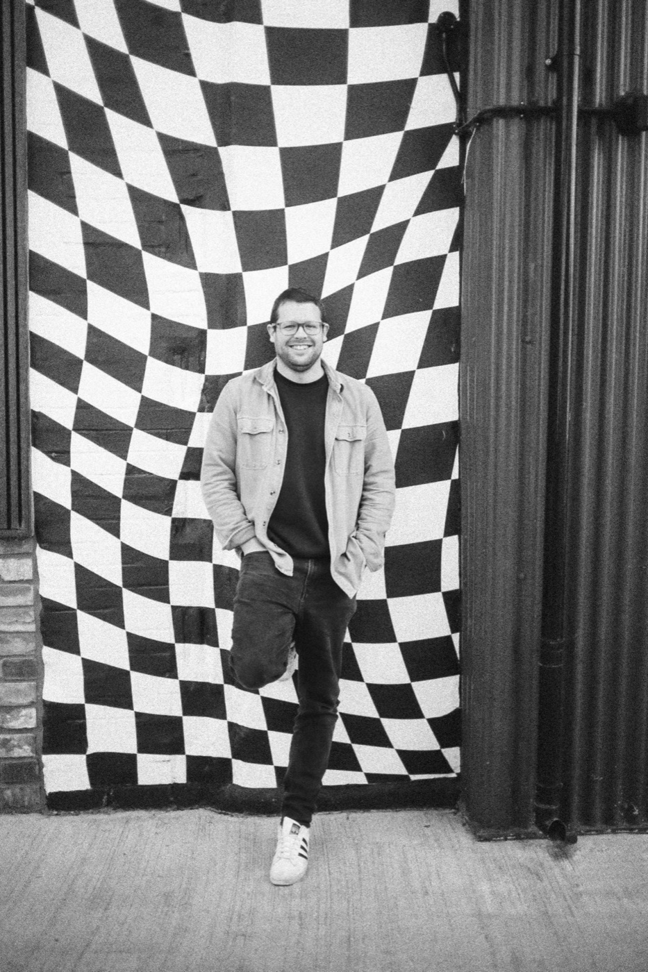 Che standing in front of a checkerboard wall, in black and white