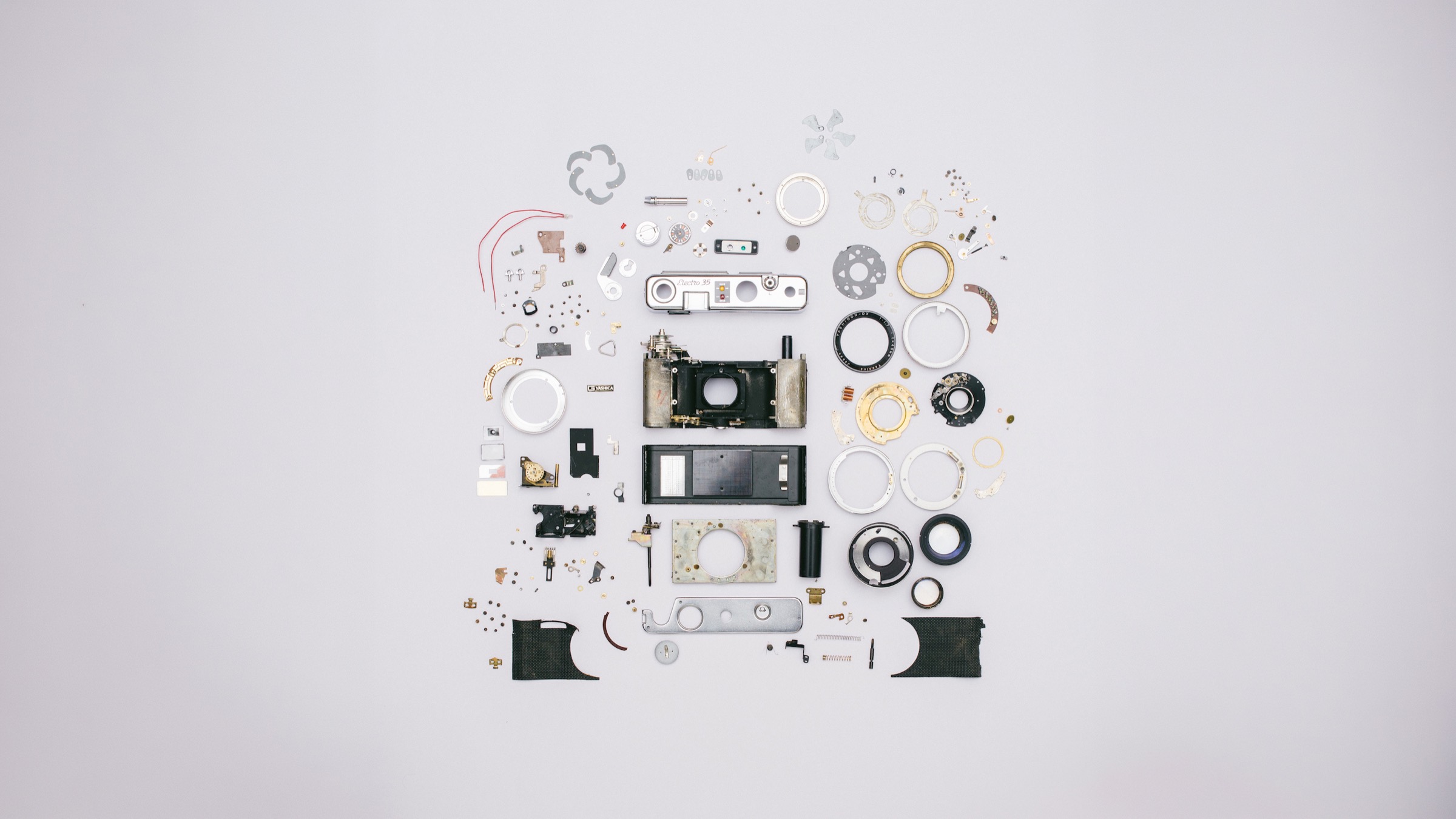 A film camera dismantled and laid out piece by piece on a pale grey surface