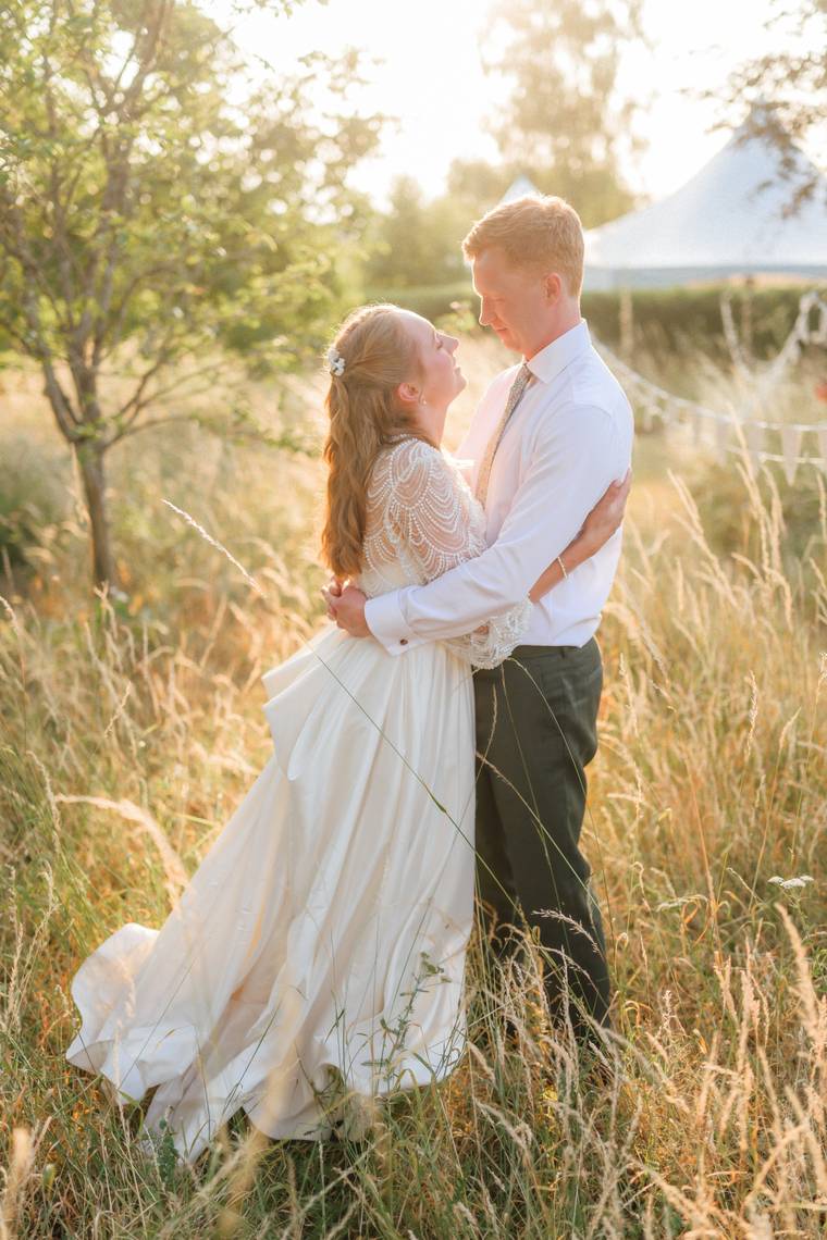 A couple standing close in a golden meadow at sunset