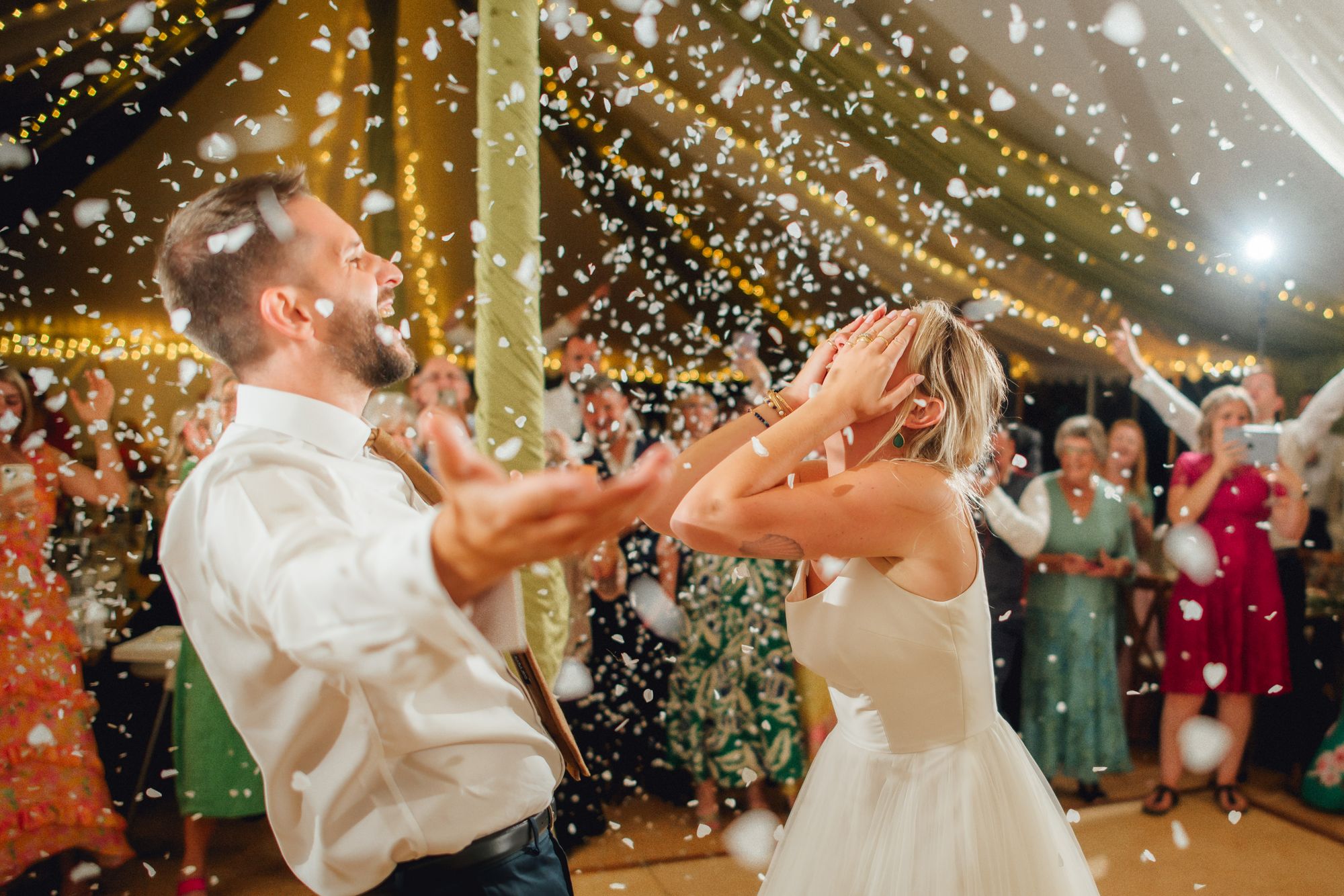 Confetti bursting over the couple mid-celebration in a fairy-lit marquee