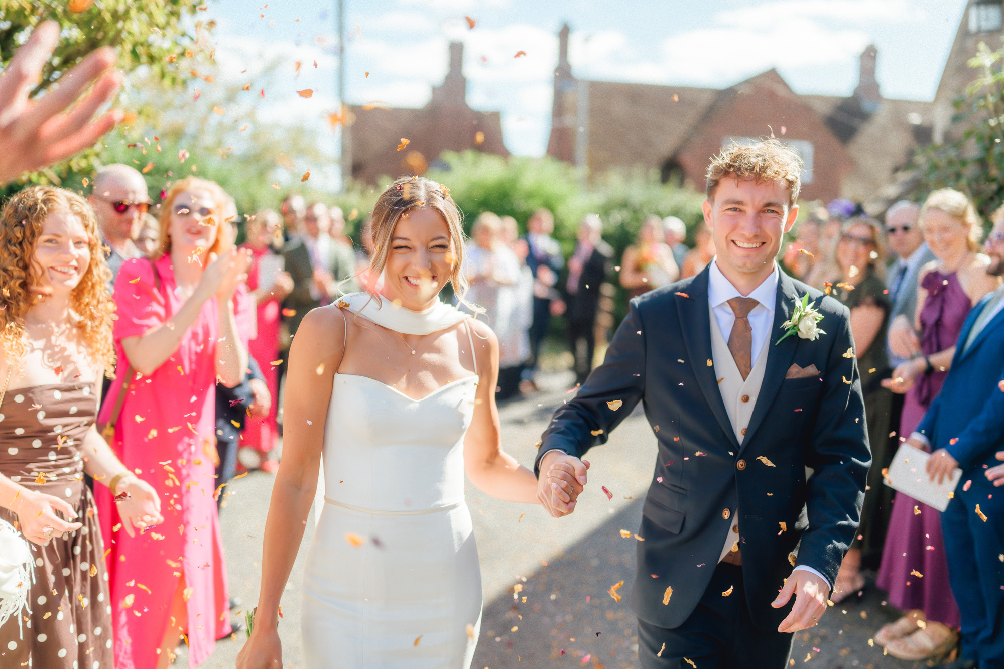 Ben and Liv walking through a shower of confetti between two lines of guests